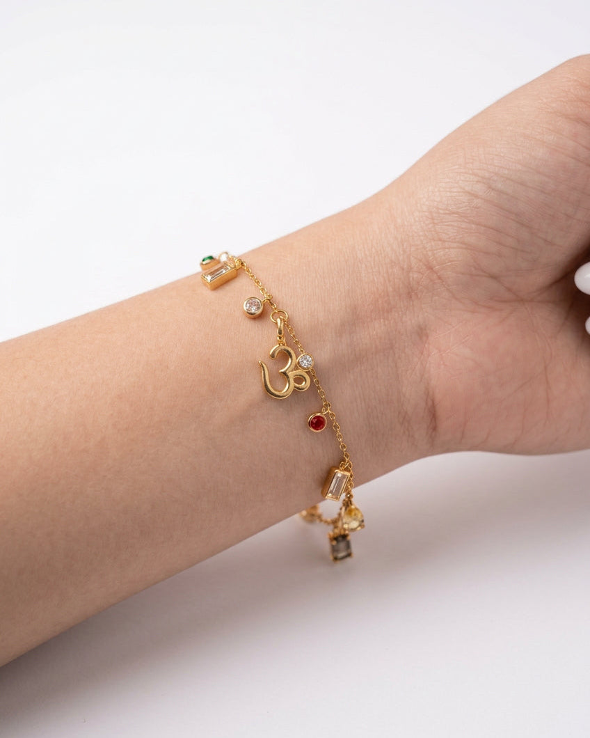 A gold-plated stainless steel bracelet with a Om symbol and small colorful gemstone charms, shown worn on a person's wrist. 