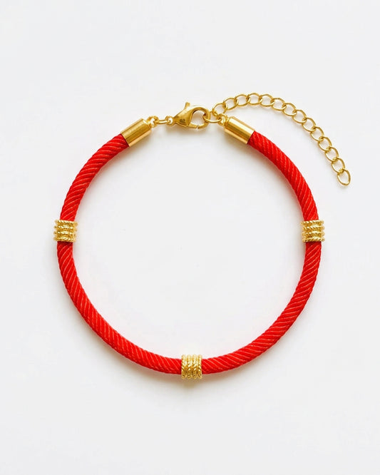 A red braided cord bracelet with gold-toned metal accents, including textured spacers and a lobster clasp with an extension chain, shown on a plain white background.