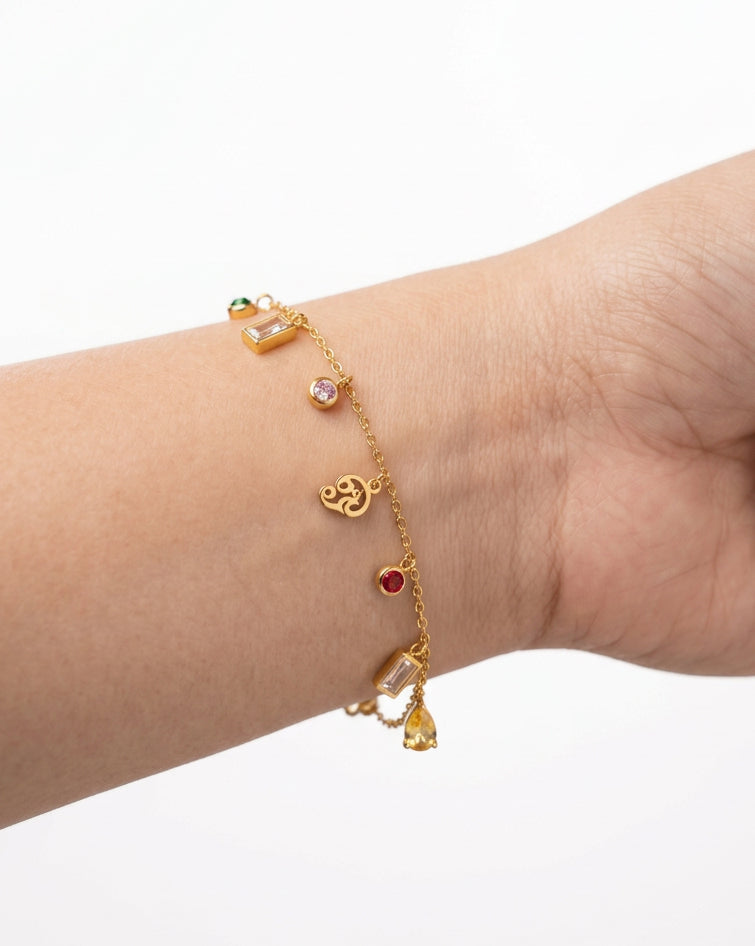 A gold-plated stainless steel charm bracelet with small decorative charms and clear gemstones, shown worn on a person's wrist.